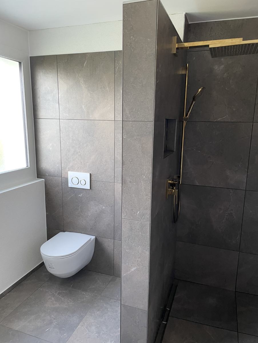 Dusche mit Natursteinfliesen und goldener Armatur