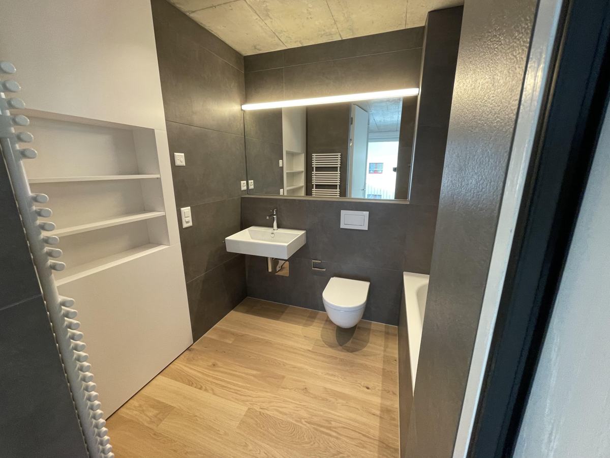 Bad mit Holzboden, grauen Wandfliesen und Handtuchradiator